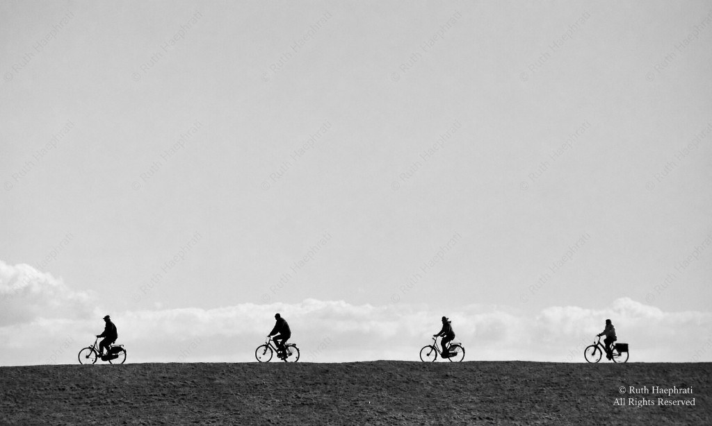 Silhouetted cyclists riding along a ridge against an open sky