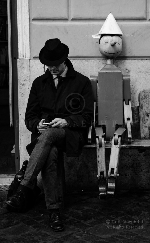 Man on a bench beside a life-sized Pinocchio puppet